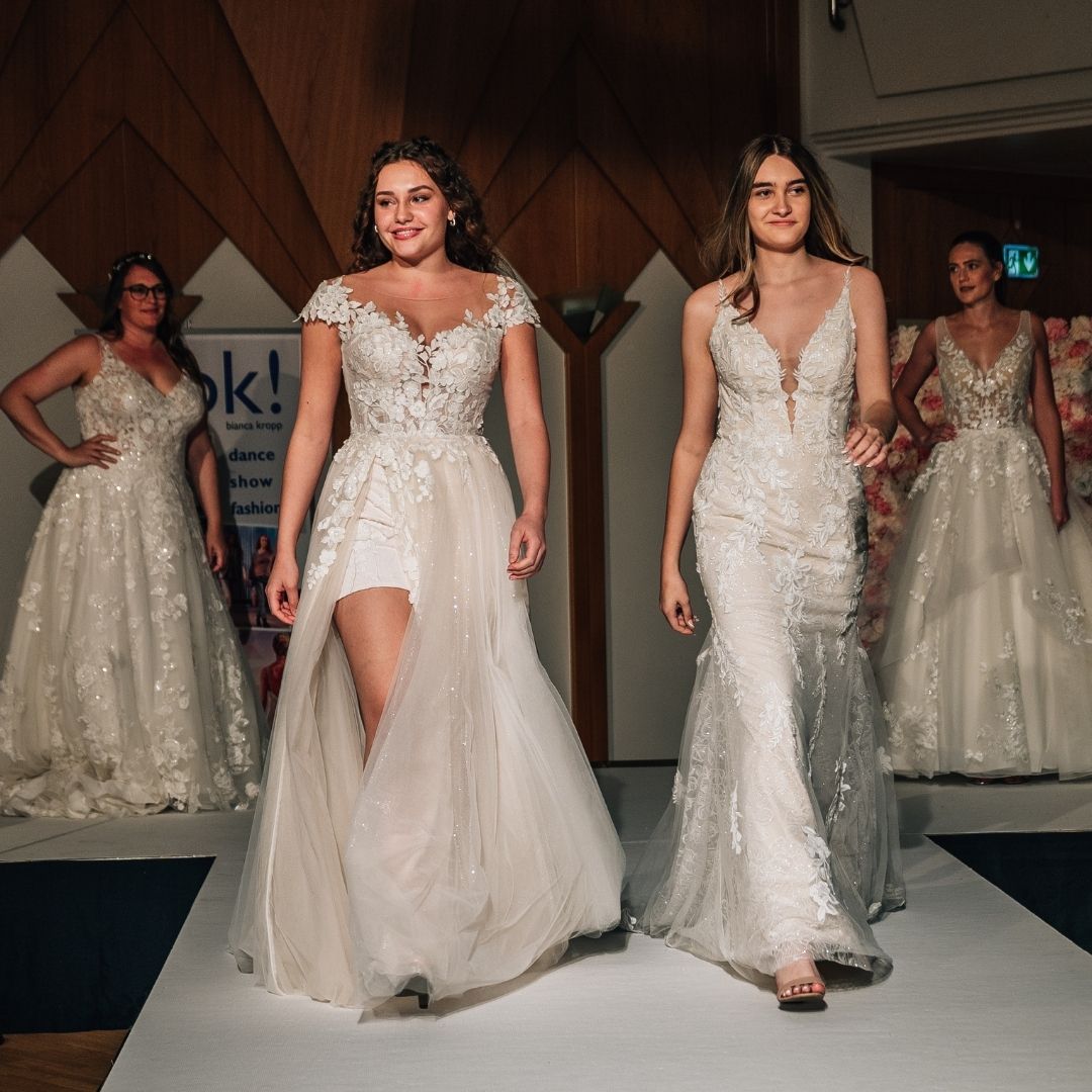 2 Models im Brautkleid laufen über einen Steg auf der Hochzeitsmesse, zwei weitere stehen im Hintergrund und lächeln.